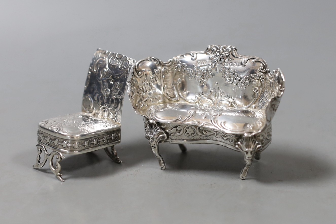 An Edwardian silver miniature model of a two seater settee, import marks for Elly Isaac Miller, London, 1902, width 68mm and a similar model of a chair, import marks for Eustace George Parker, London, 1897.